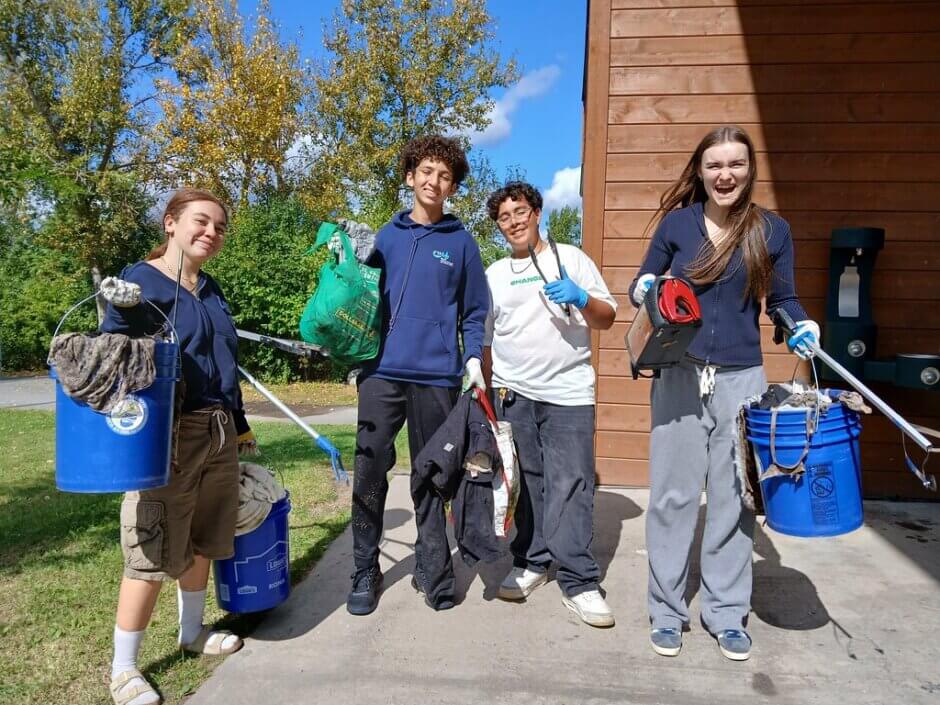 Four youth holding up bags or buckets of trash and smiling and laughing. 