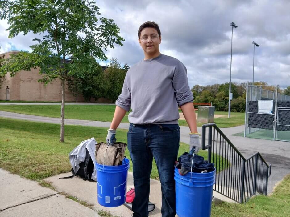A student carrying two buckets full of garbage while looking at the camera. 