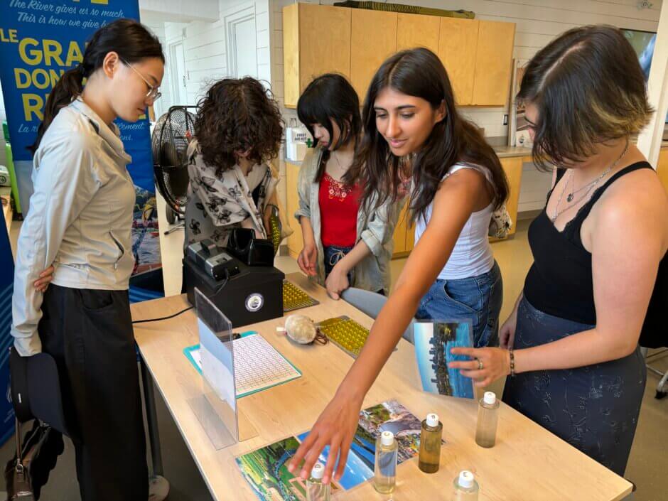 Youth looking at a table in the Learning Lab covered in activities and information, including bottles of different types of river water. 