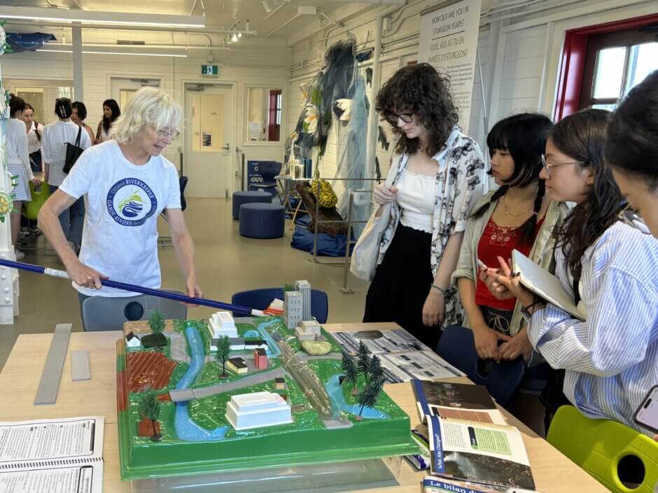 A volunteer in an Ottawa Riverkeeper shirt showing four youth the watershed model on a table in the Learning Lab. 